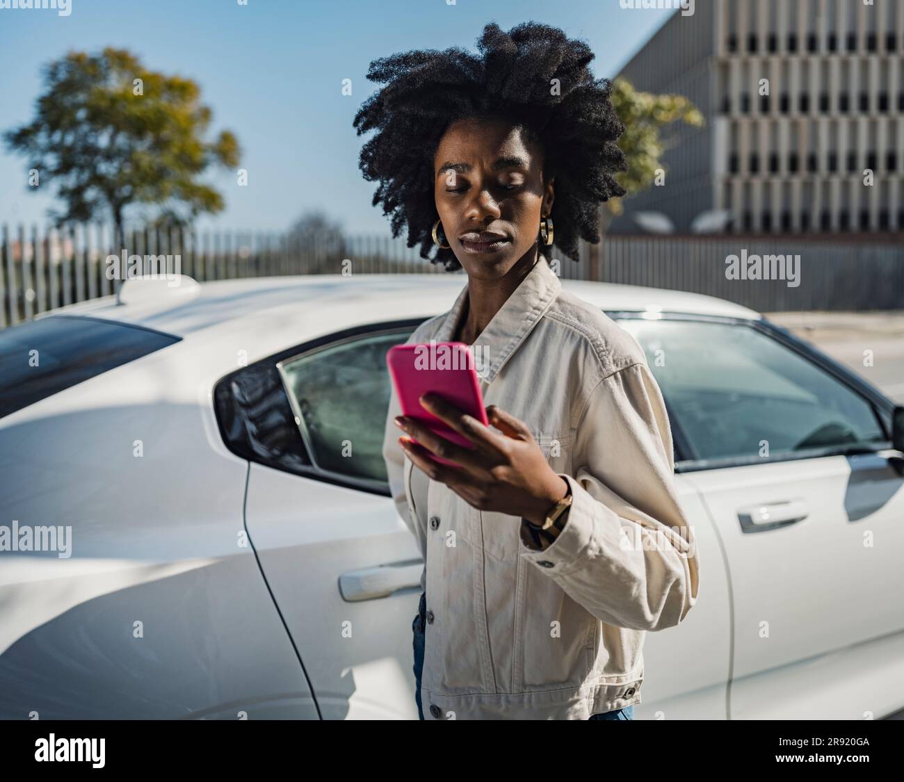 Young woman using smart phone standing by white car Stock Photo