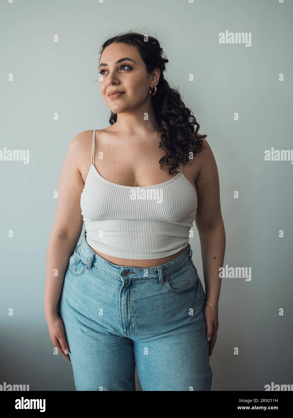 Thoughtful curvy woman standing in front of wall Stock Photo - Alamy