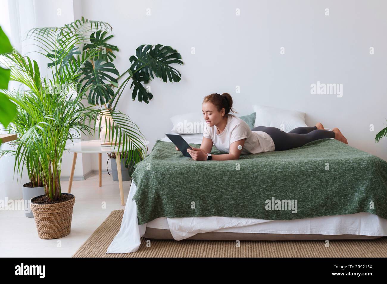 Young woman with diabetes using tablet PC lying on bed at home Stock Photo