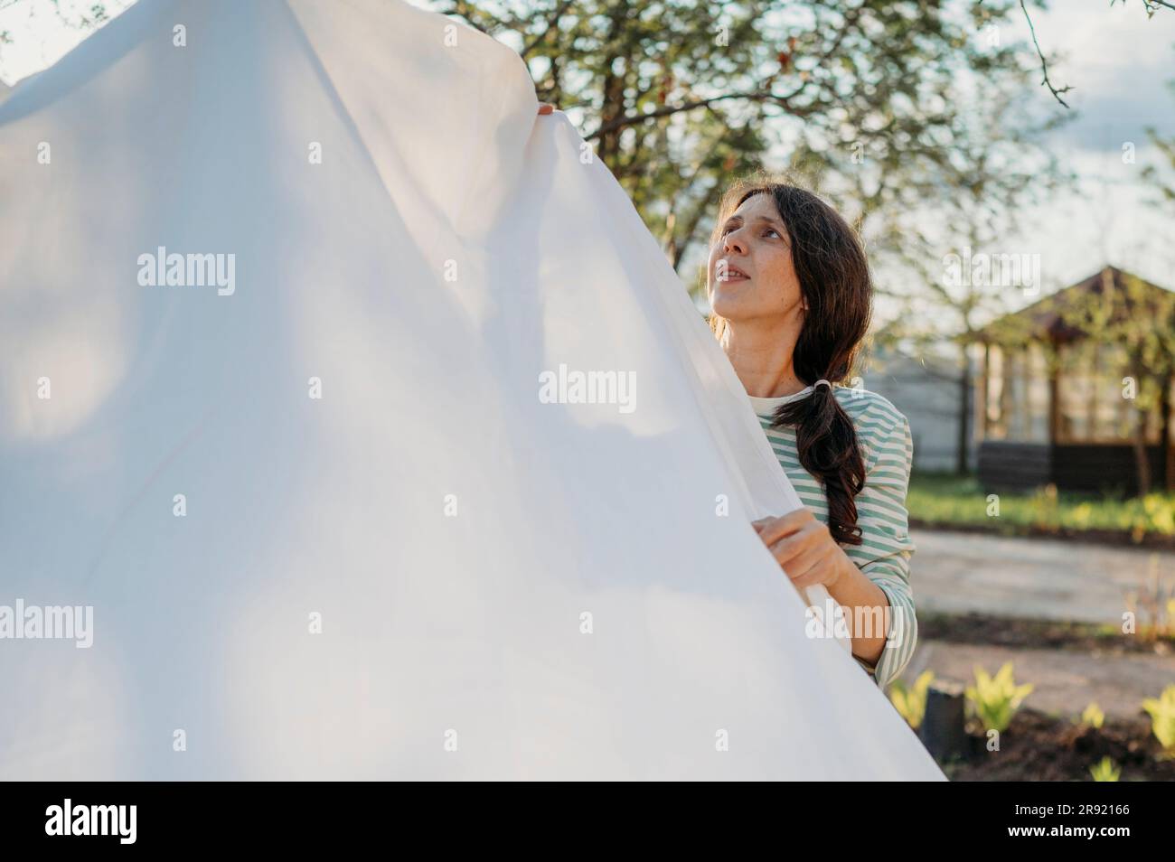 Woman drying white bedding sheet on clothesline in back yard Stock Photo