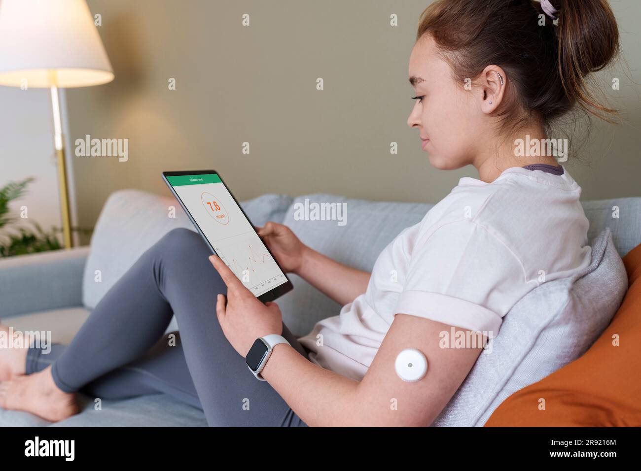 Woman using tablet PC with diabetes glucose sensor on arm at home Stock Photo