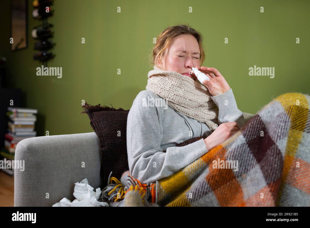Sick young woman using nasal spray relaxing on couch Stock Photo