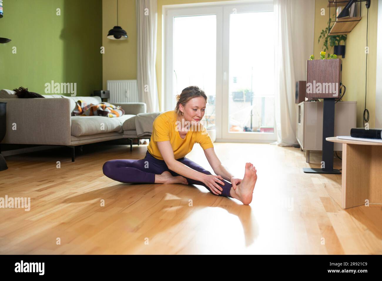 Smiling woman in yellow T-shirt and purple leggings exercising at home Stock Photo