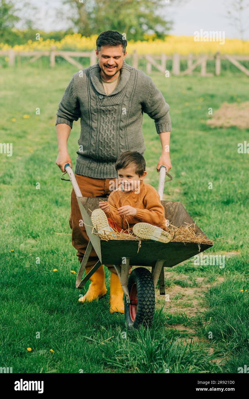 Playful father pushing son sitting in wheelbarrow at garden Stock Photo