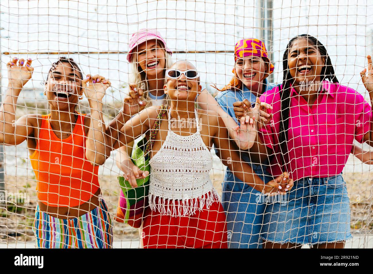 Happy multiracial friends standing behind net Stock Photo - Alamy