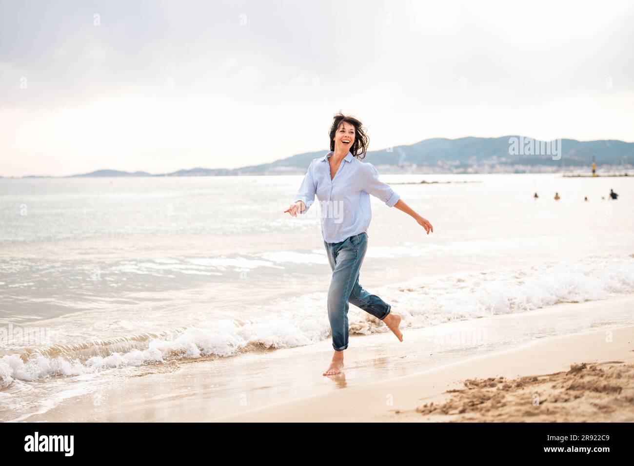 Carefree woman running near shore at beach Stock Photo