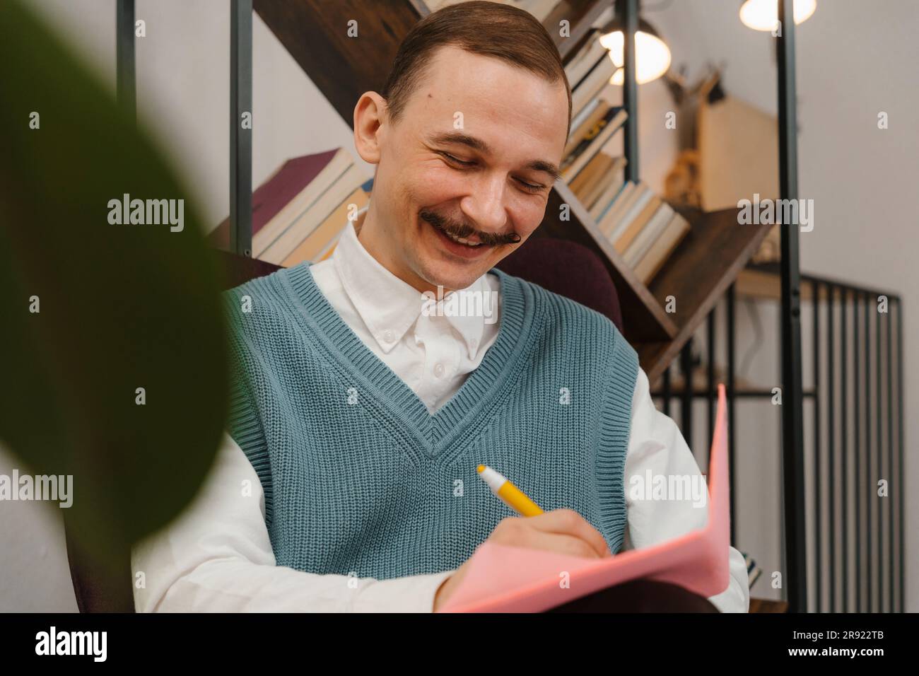 Smiling man with moustache taking notes sitting in studio Stock Photo