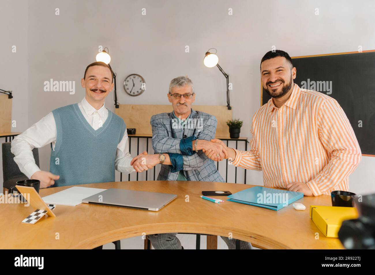 Three male colleagues of different ages and nationalities shaking hands in studio Stock Photo
