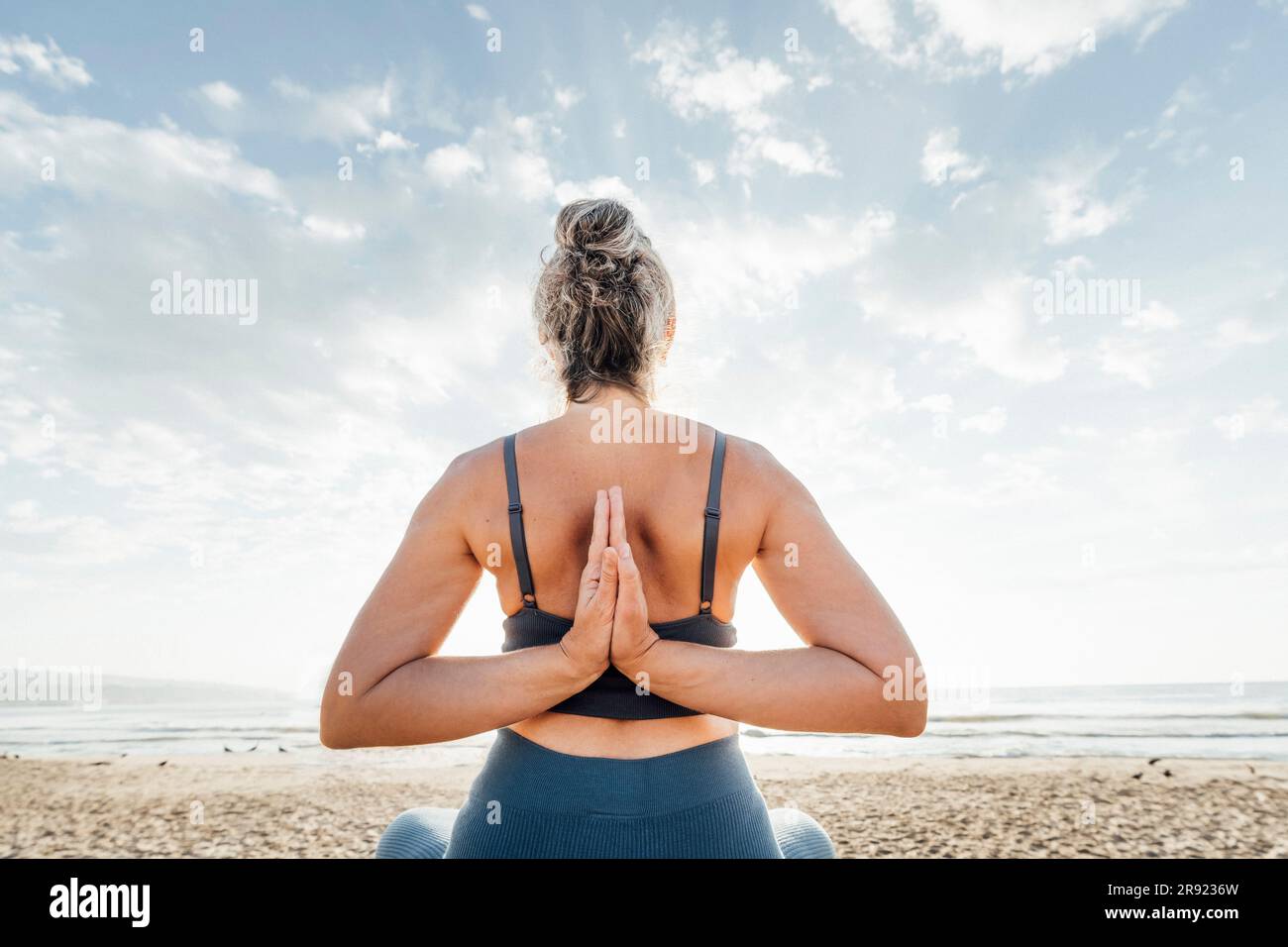 Woman practicing yoga with hands clasped behind back sitting at beach Stock Photo