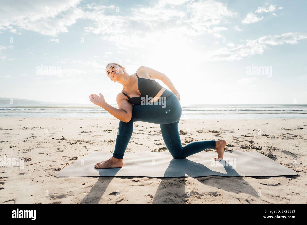 Woman exercising on mat at beach Stock Photo