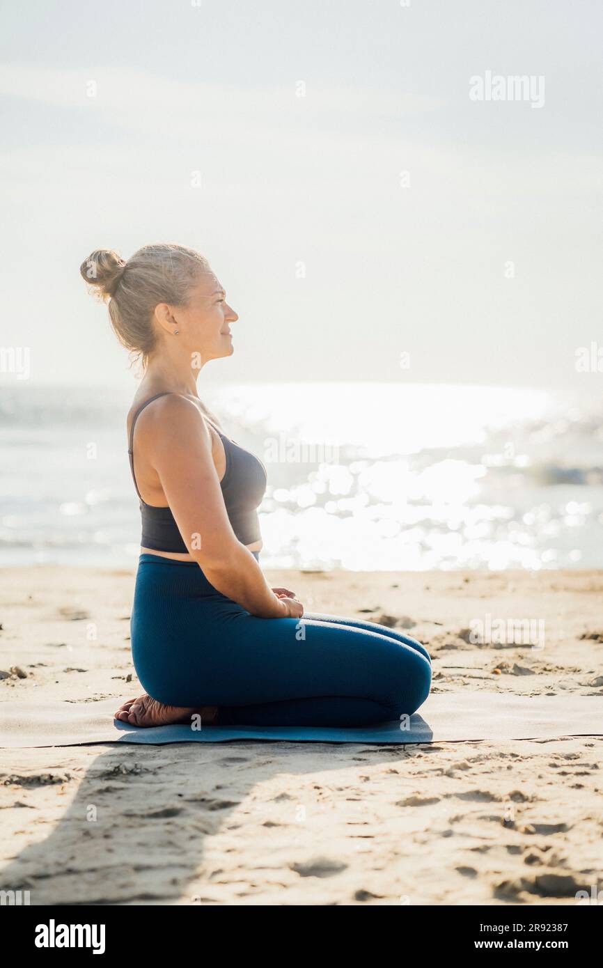 Woman practicing breathing exercise on beach at sunny day Stock Photo