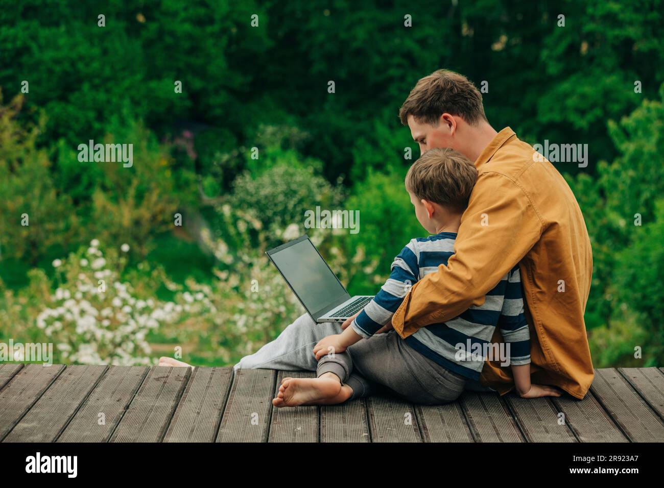 Son with father using laptop on boardwalk Stock Photo