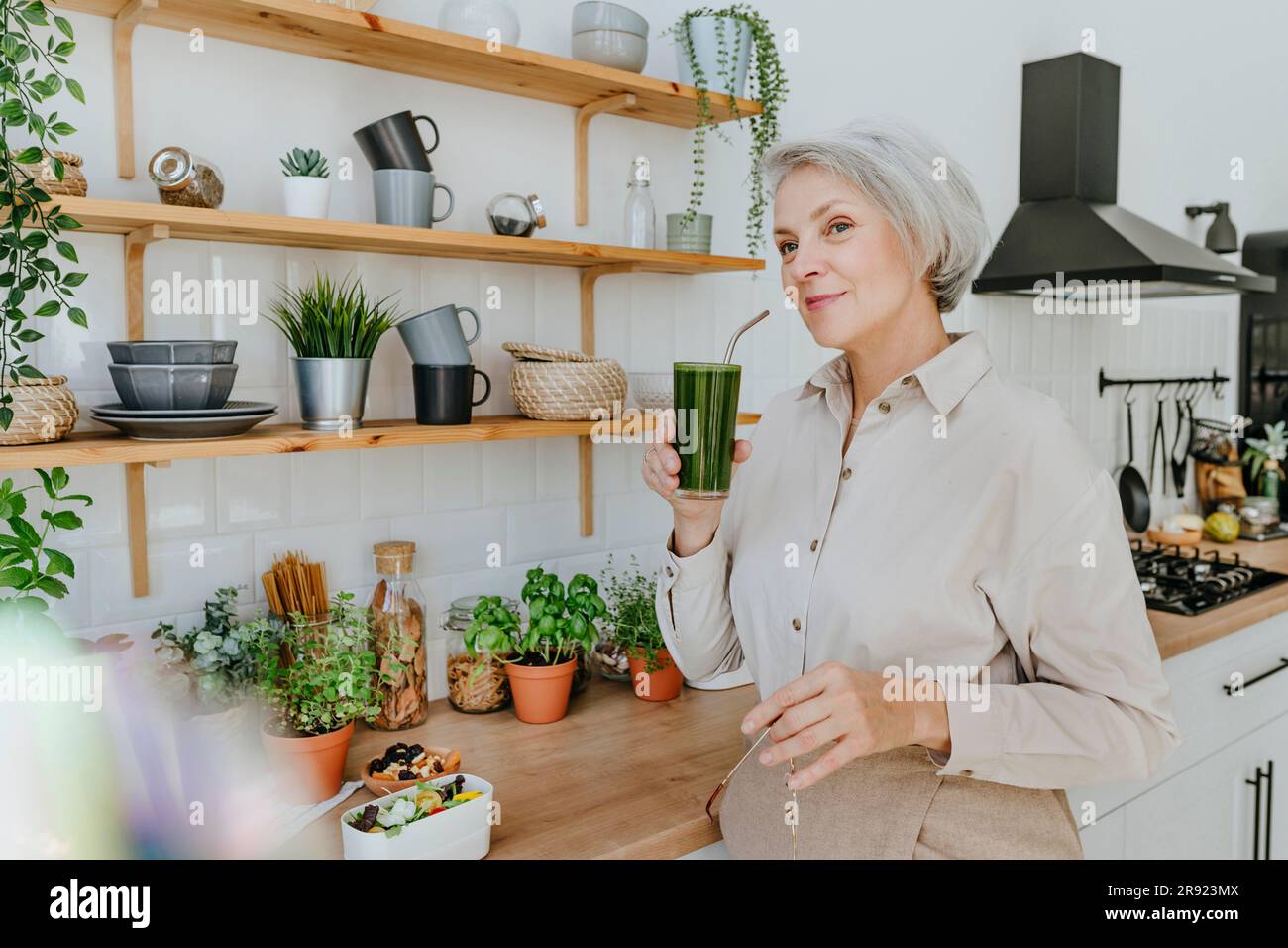Smiling woman drinking detox juice in kitchen at home Stock Photo