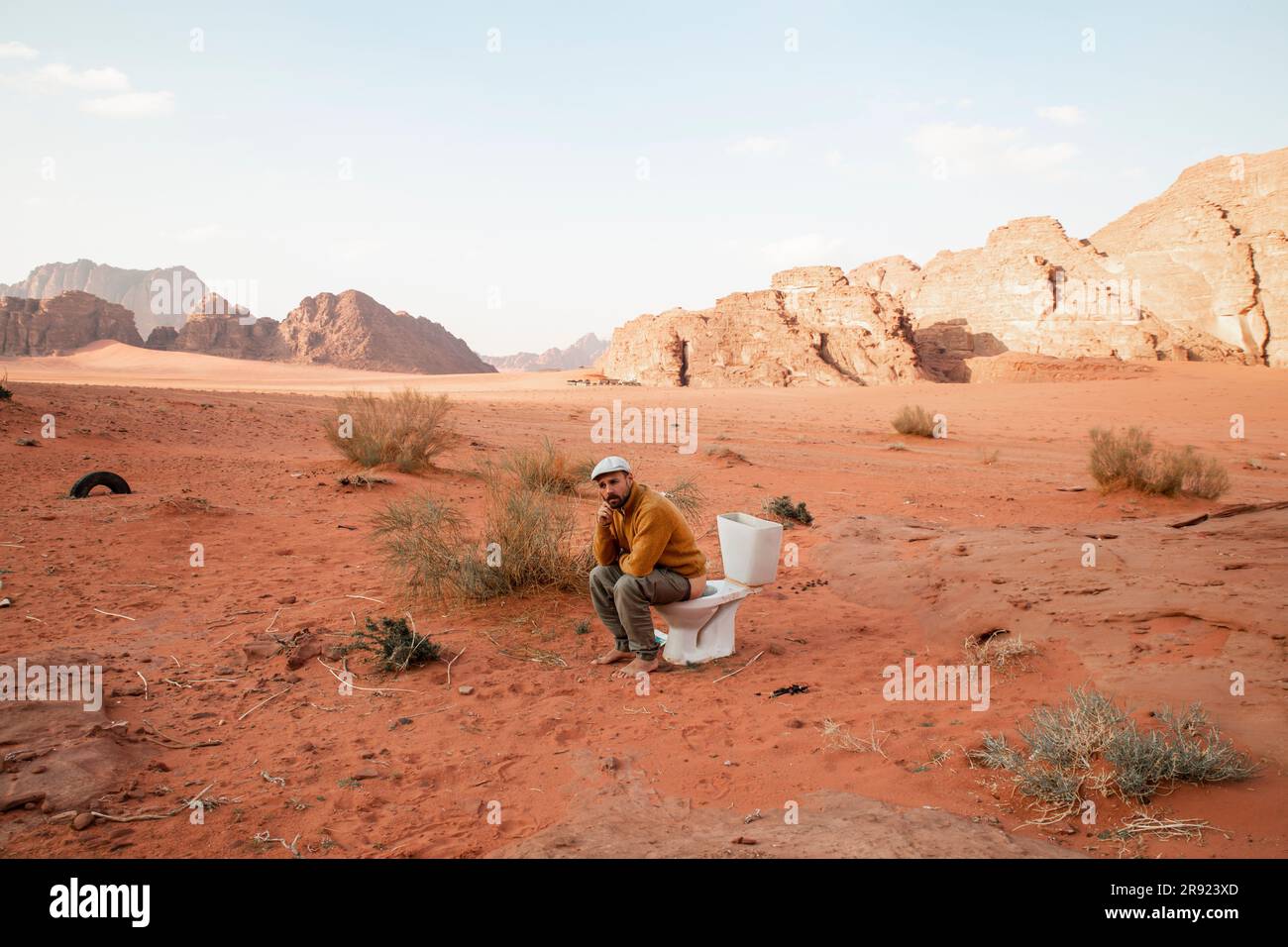 Thoughtful man sitting on toilet seat and defecating in desert Stock Photo
