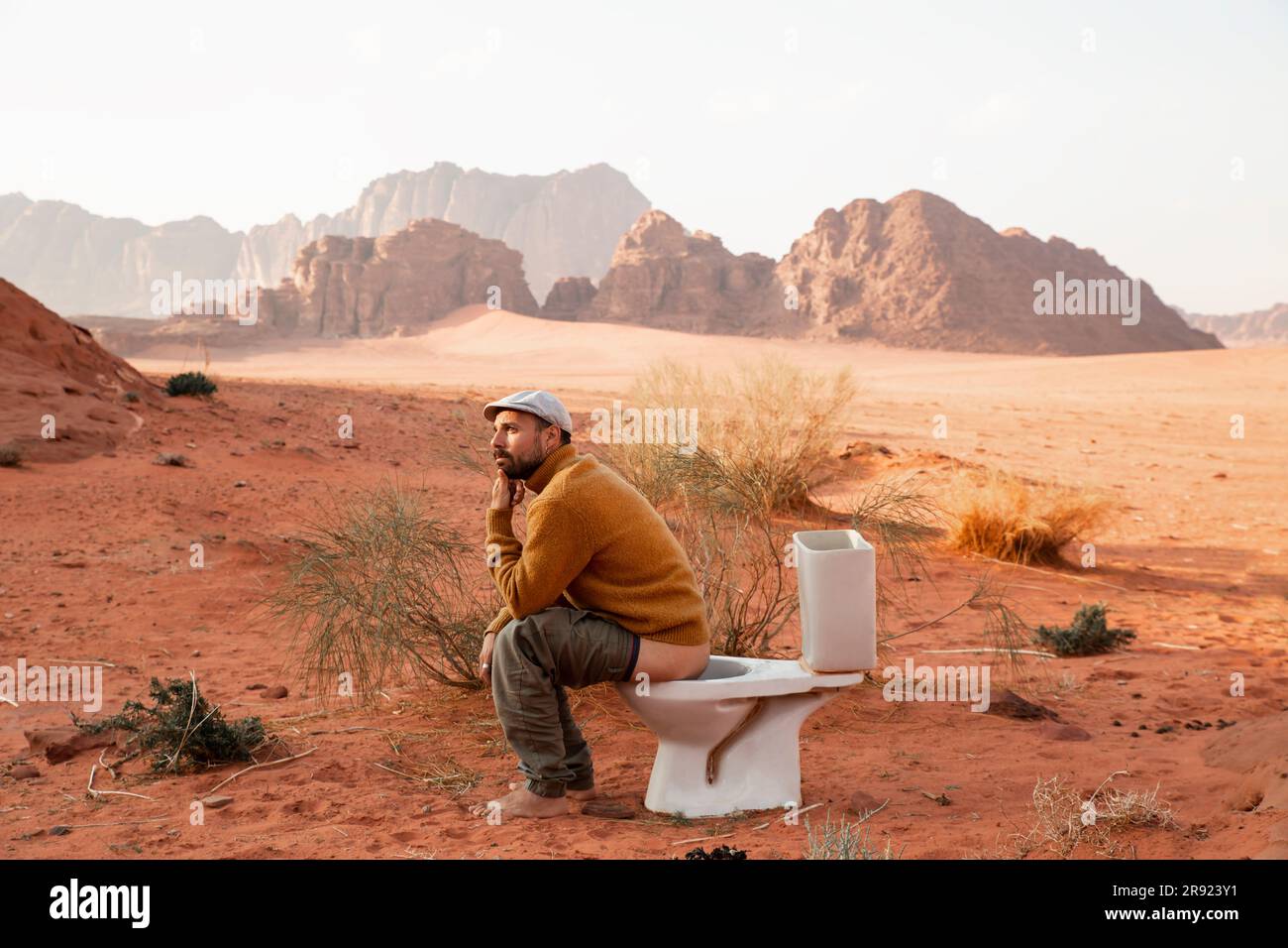 Contemplative man sitting on toilet seat and defecating in desert Stock Photo