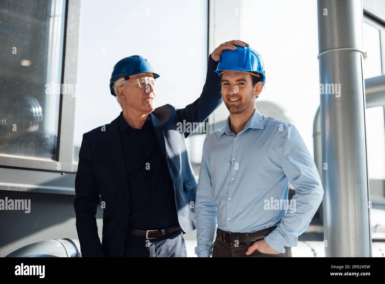 Happy engineers wearing hardhats standing at industry Stock Photo