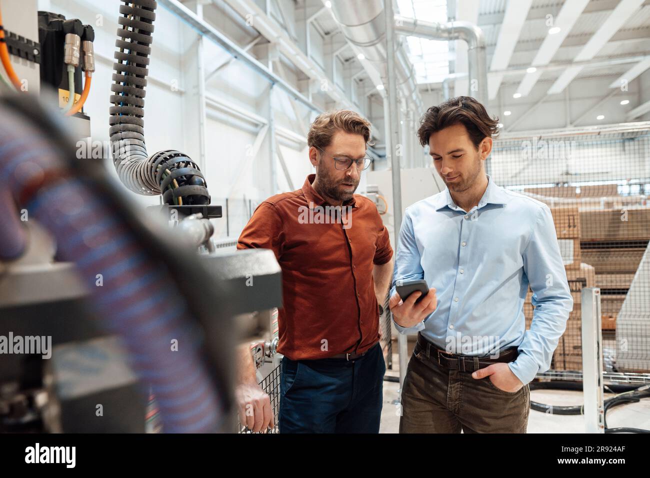 Businessmen discussing over smart phone in factory Stock Photo - Alamy