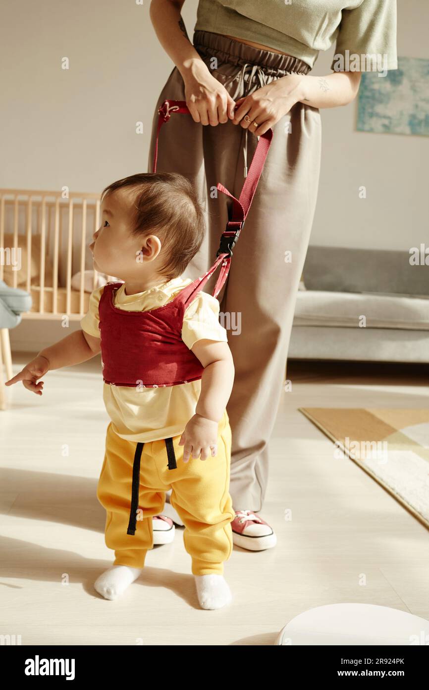 Mother supporting daughter learning to walk at home Stock Photo