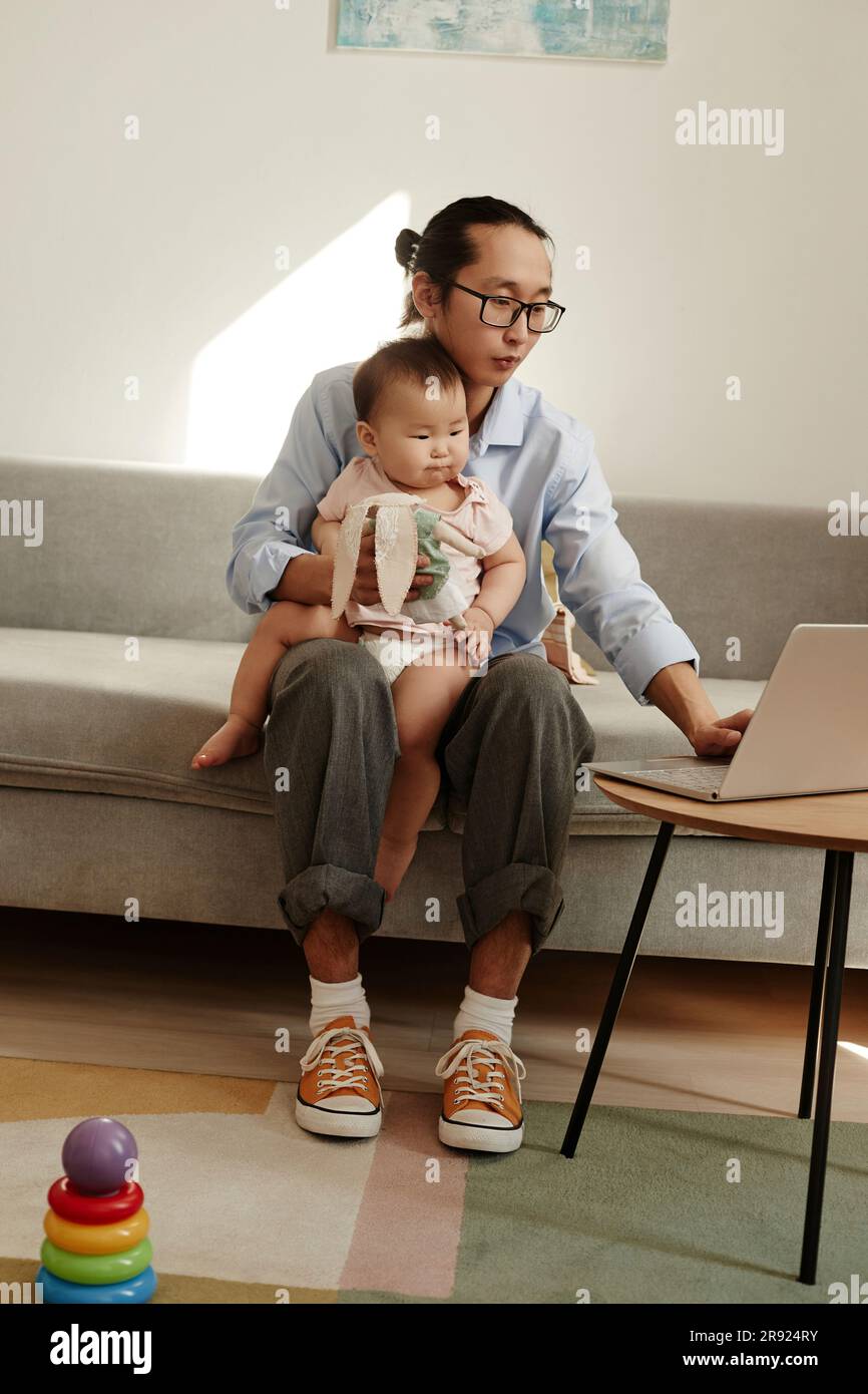 Freelancer father working on laptop sitting with daughter at home Stock Photo