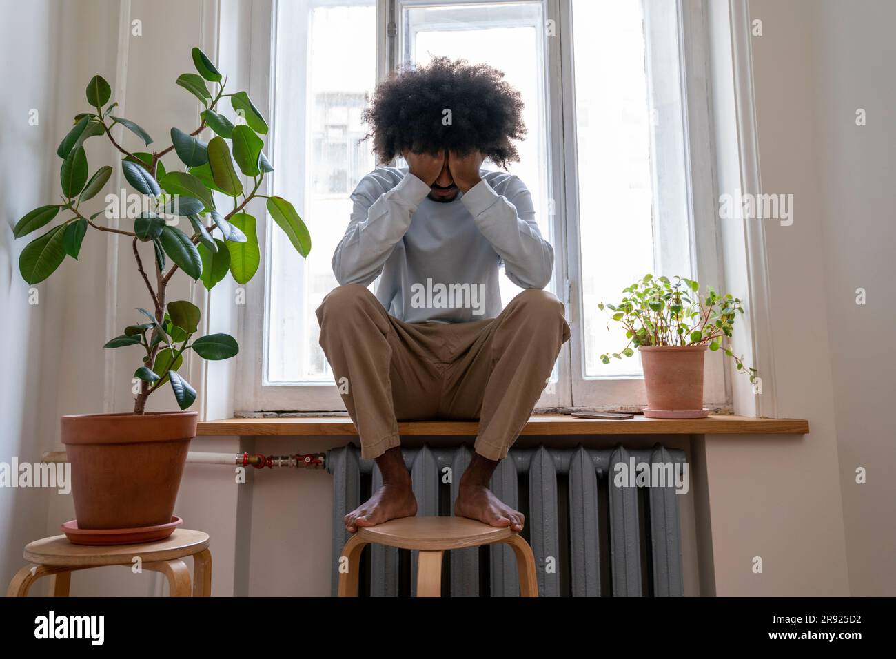 Depressed man sitting on window sill at home Stock Photo
