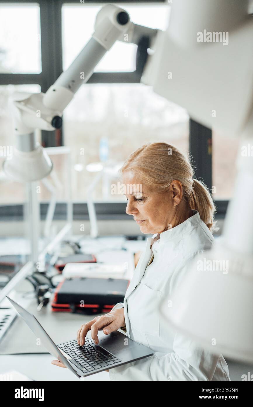Scientist using laptop by robotic arms in laboratory Stock Photo