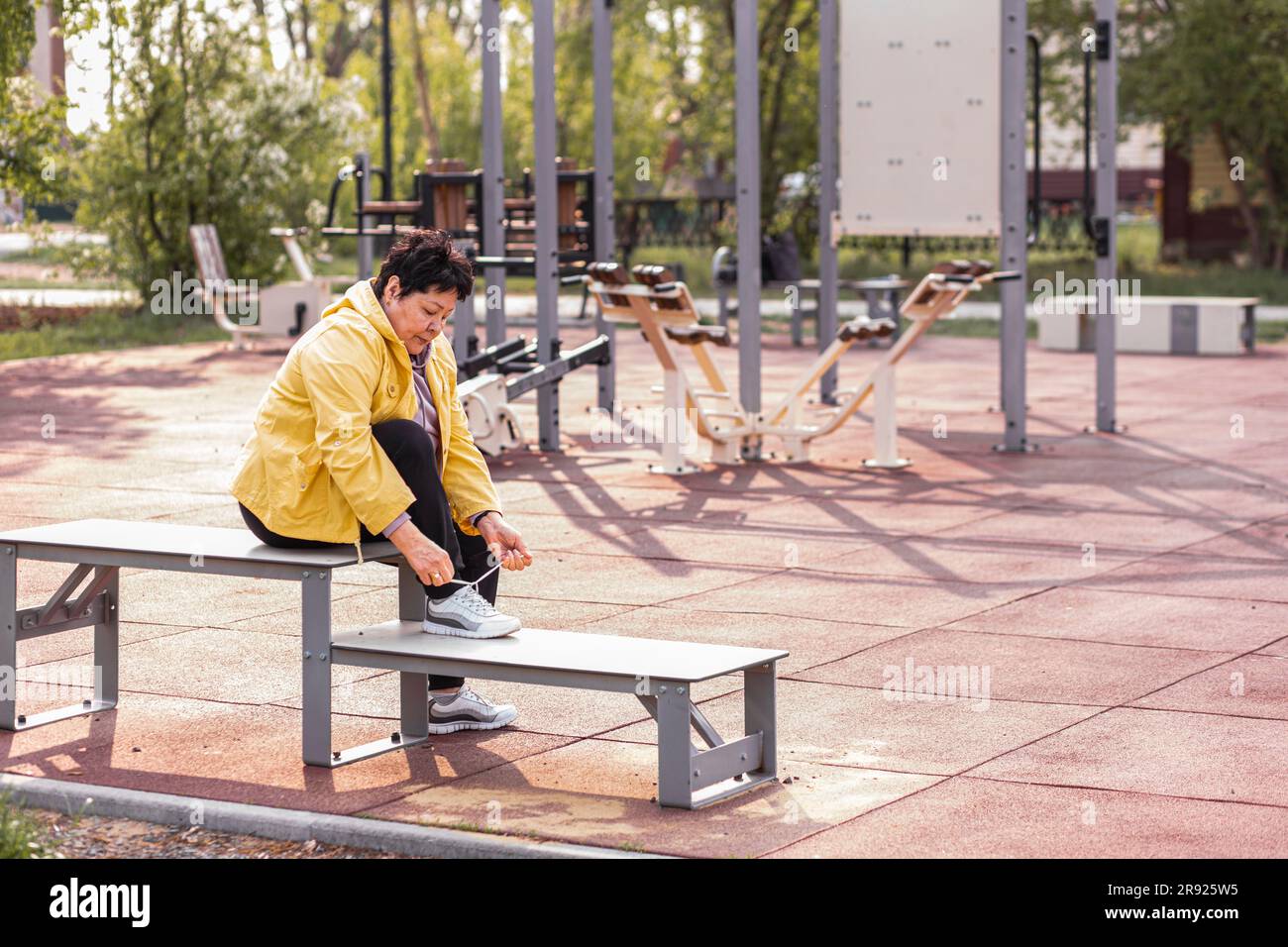 Senior woman tying shoelace sitting on bench at park Stock Photo