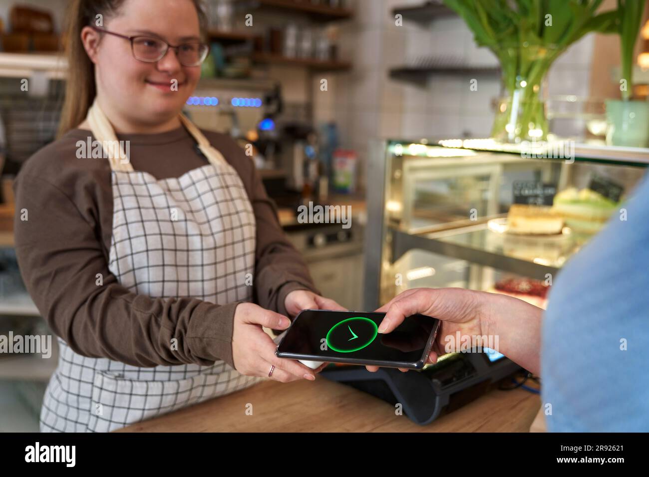 Smiling cafe owner with down syndrome and customer making payment through mobile phone Stock Photo