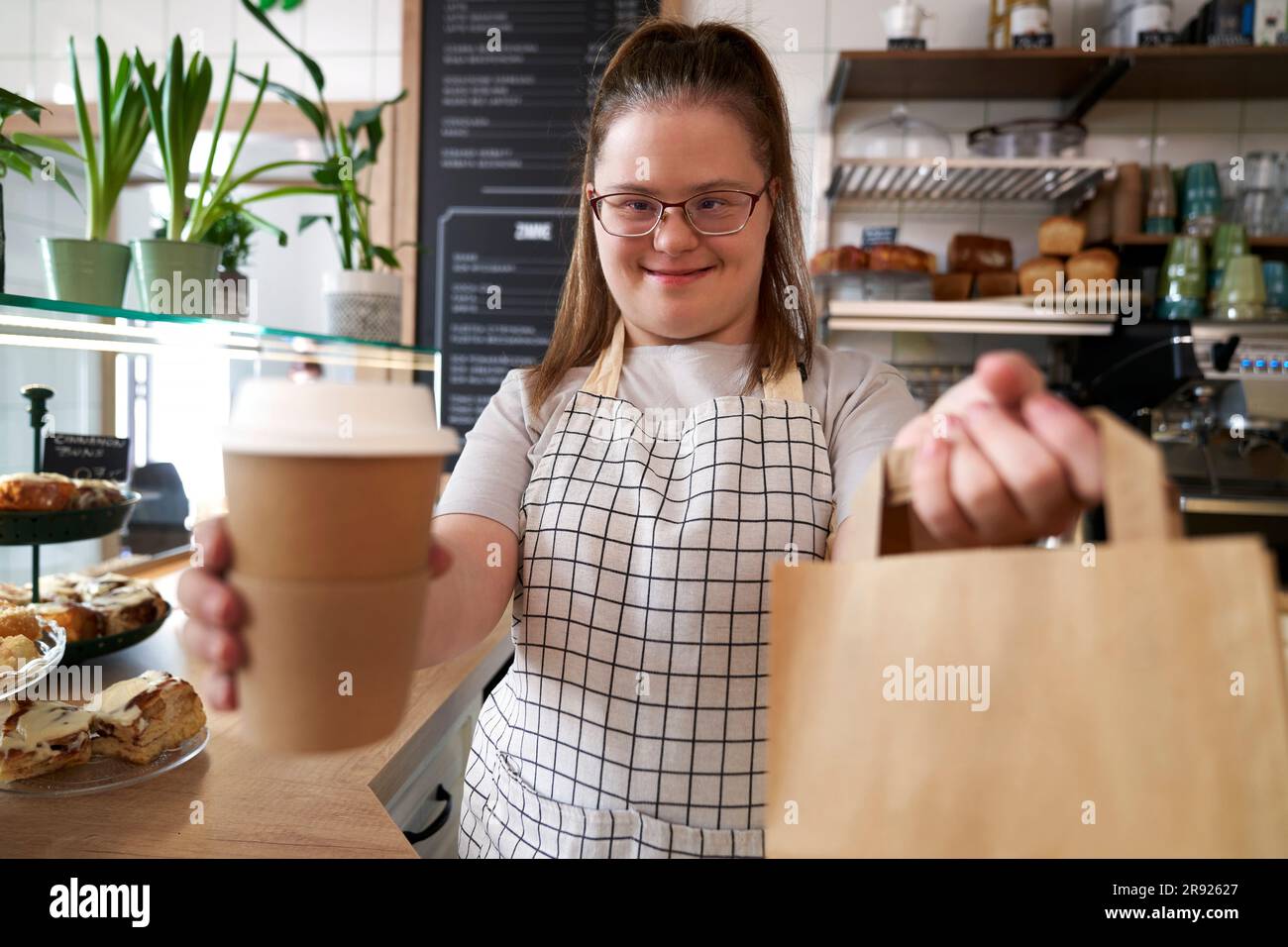 Happy cafe owner with down syndrome holding paper bag and disposable
