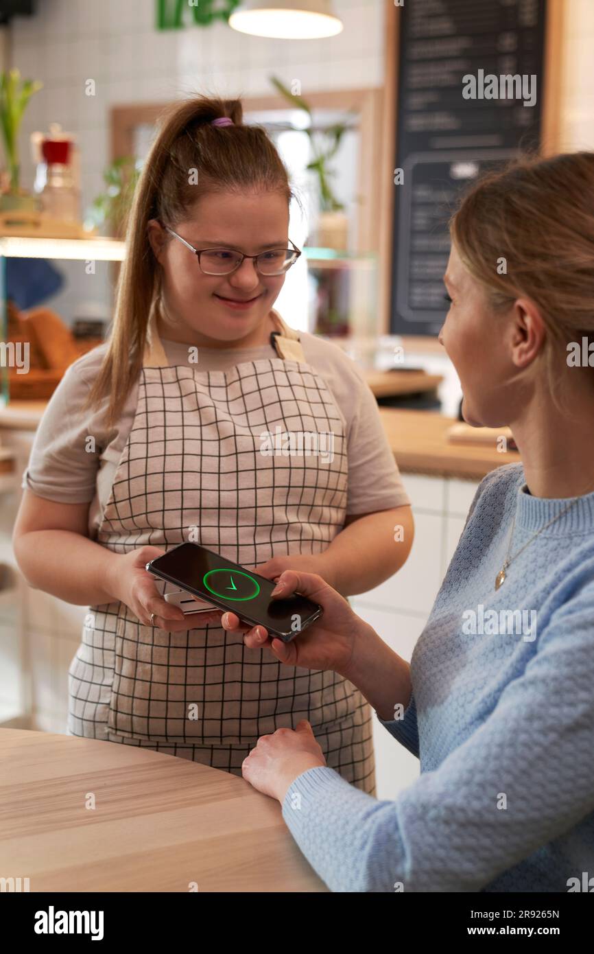 Cafe owner with down syndrome with customer doing payment in cafe Stock Photo
