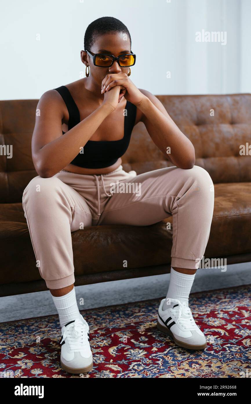 Young woman with hands clasped sitting on sofa Stock Photo