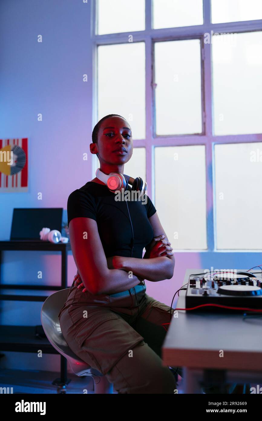 Young Dj sitting with arms crossed in studio Stock Photo