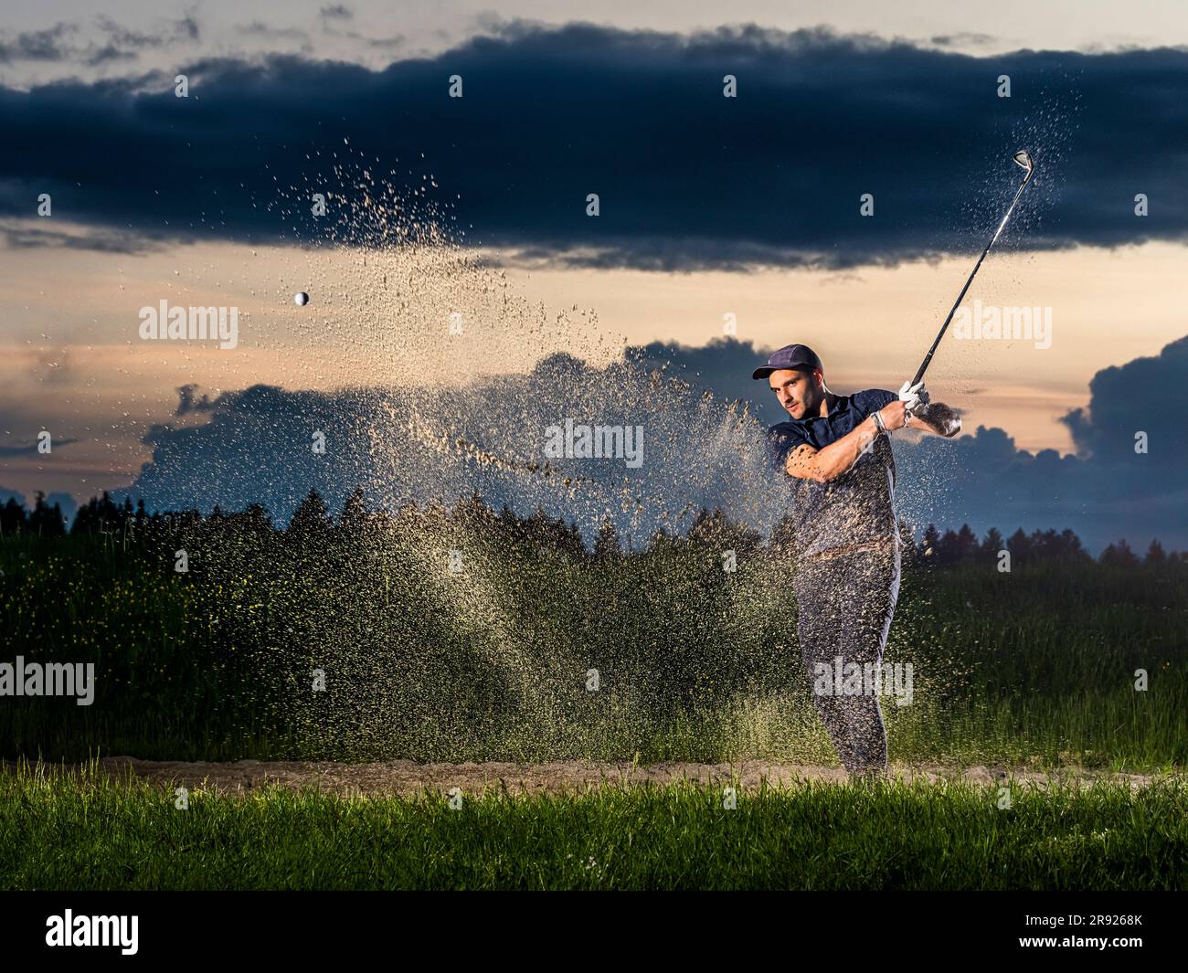 Man playing golf with club sanding on grass at dusk Stock Photo