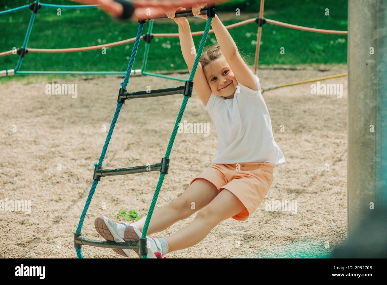 Smiling girl climbing rope ladder at playground Stock Photo