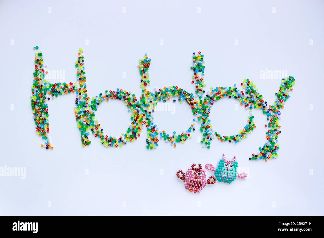The word Hobby written on a white background with multi-colored beads and two figurines of owls made of beads Stock Photo