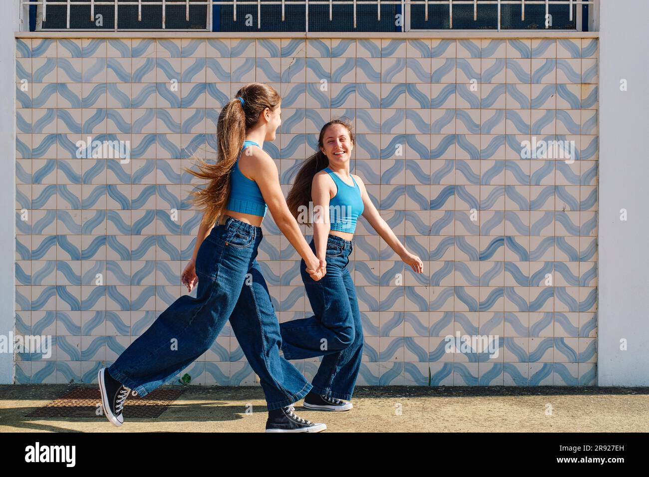 Happy girls holding hands and running in front of wall Stock Photo - Alamy