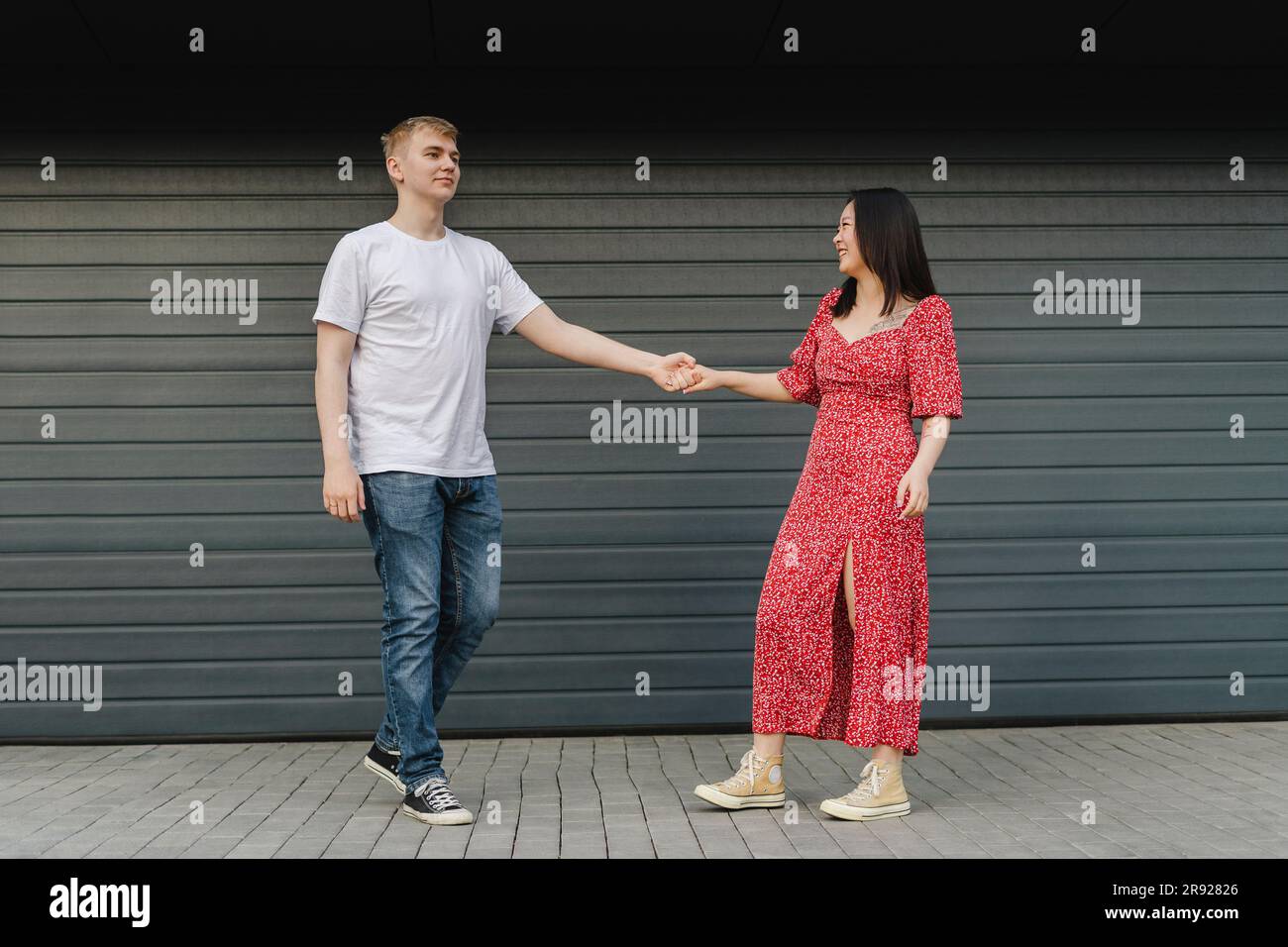 Romantic young couple holding hands in front of closed shutter Stock Photo