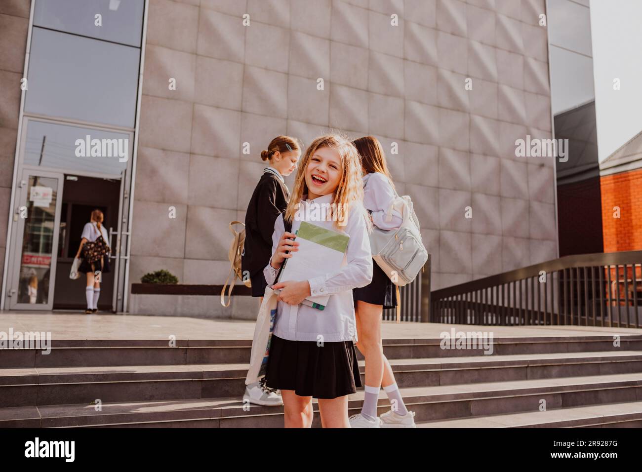 Happy girl standing in front of school building with friends in ...