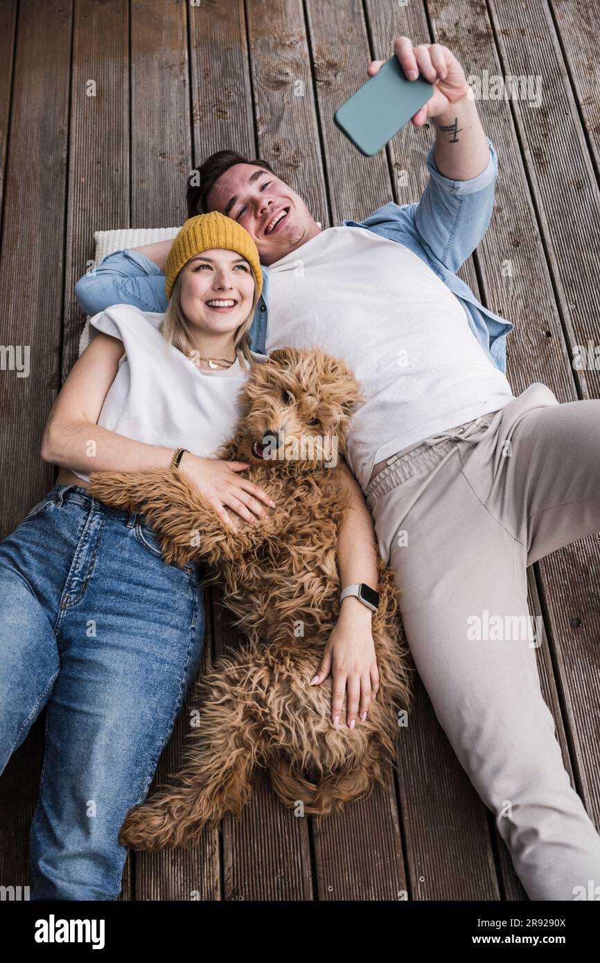 Happy young couple taking selfie with dog and lying on floor Stock Photo