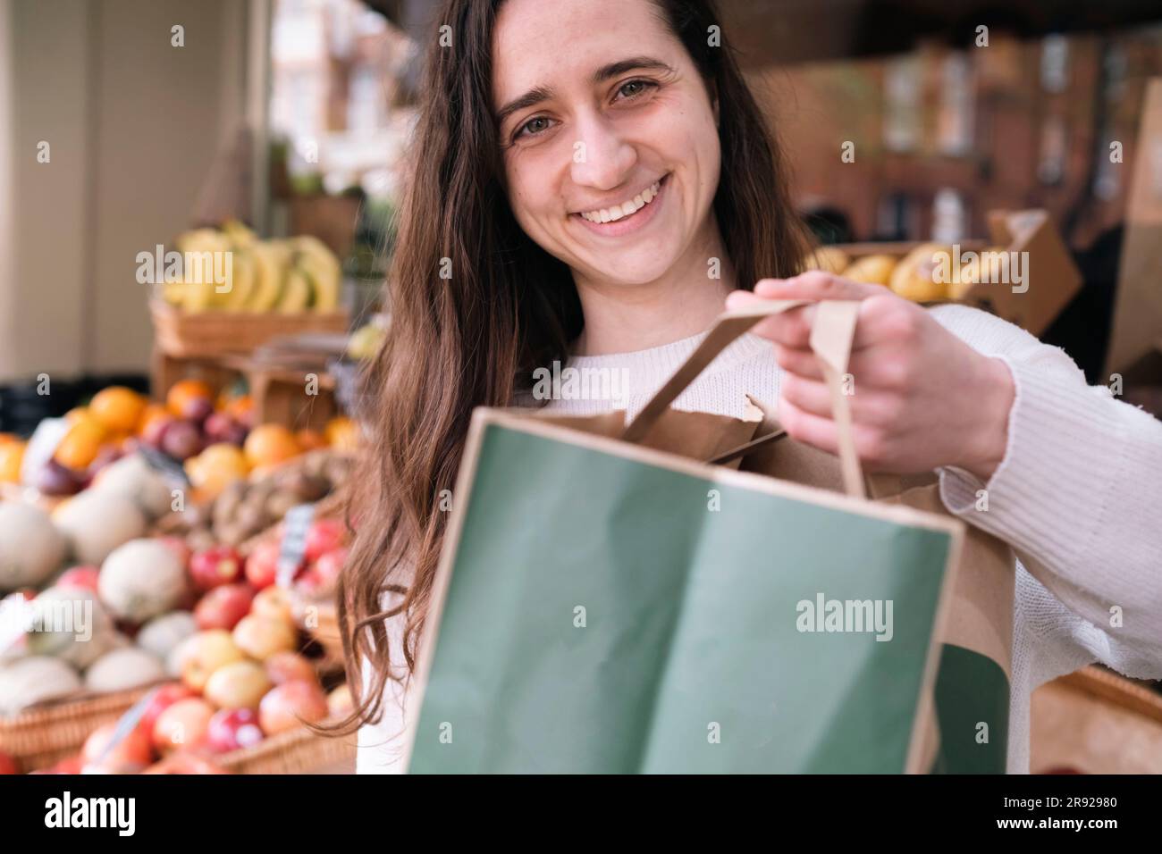 Happy young grocer standing with paper bag at vegetable stall Stock Photo Alamy