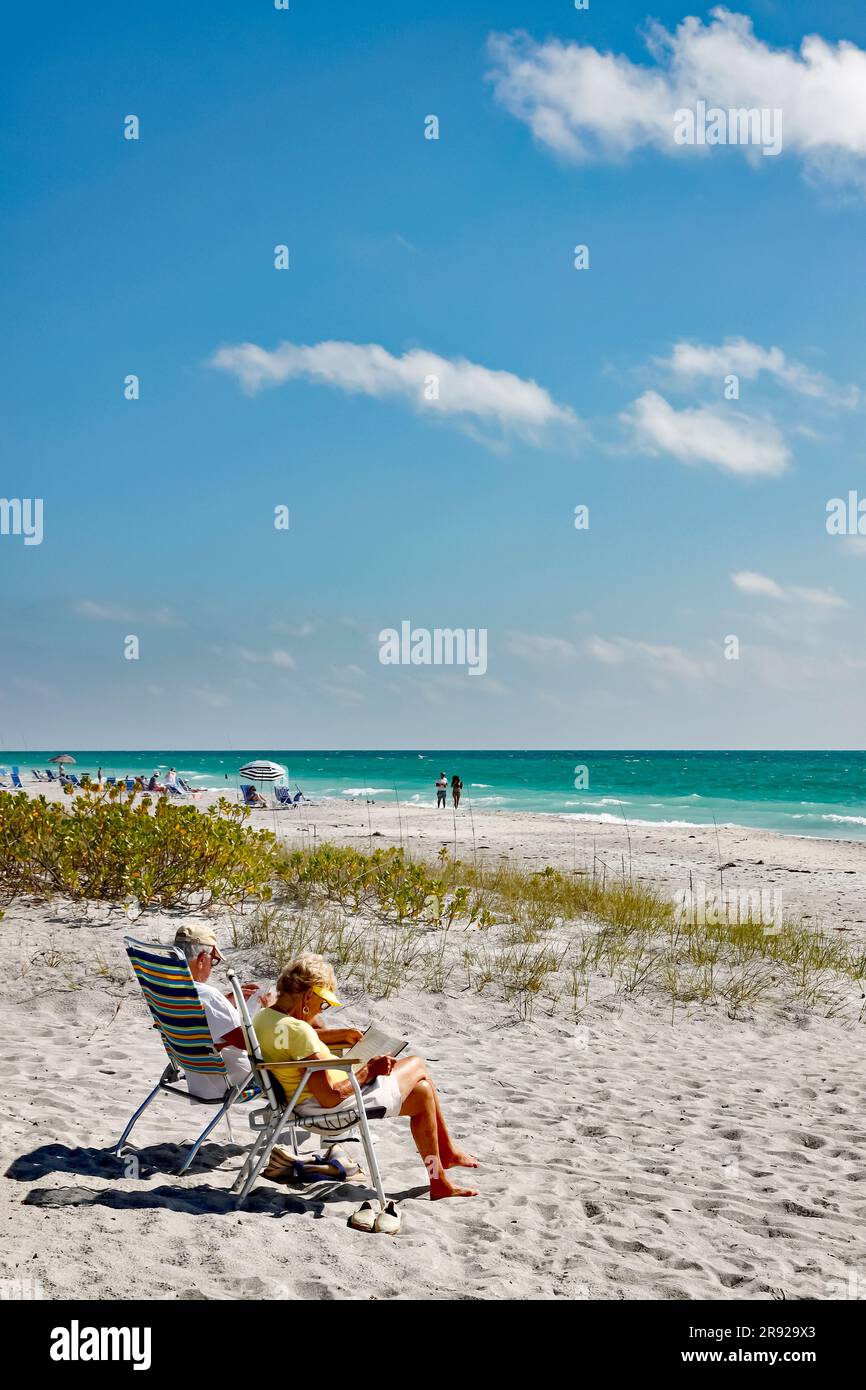 Retired senior couple reading on the beach in Siesta Key, Sarasota, the West or Gulf coast of Florida, USA. Stock Photo