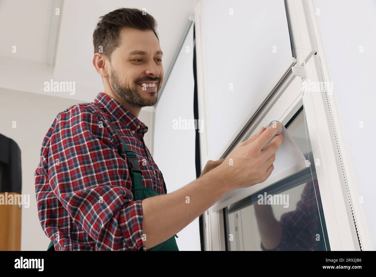 Worker in uniform installing roller window blind indoors Stock Photo