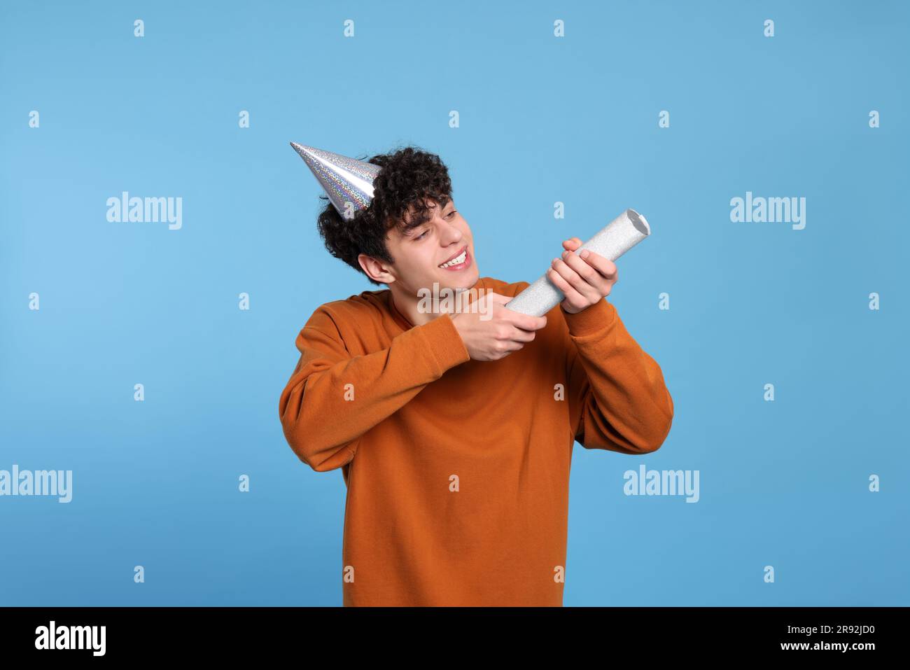 Handsome young man in party hat with popper on light blue background