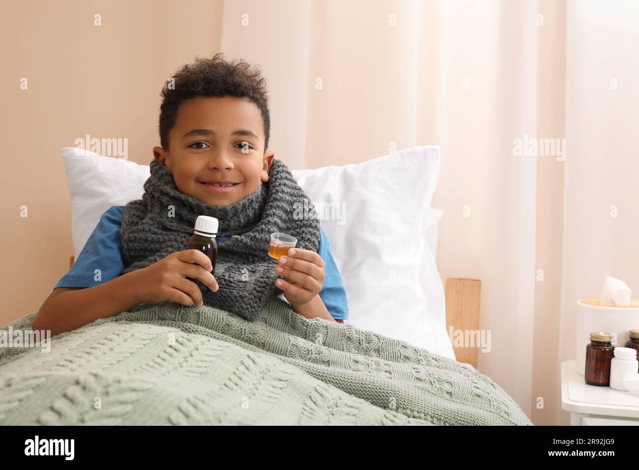 African-American boy taking cough syrup on bed at home, space for text ...