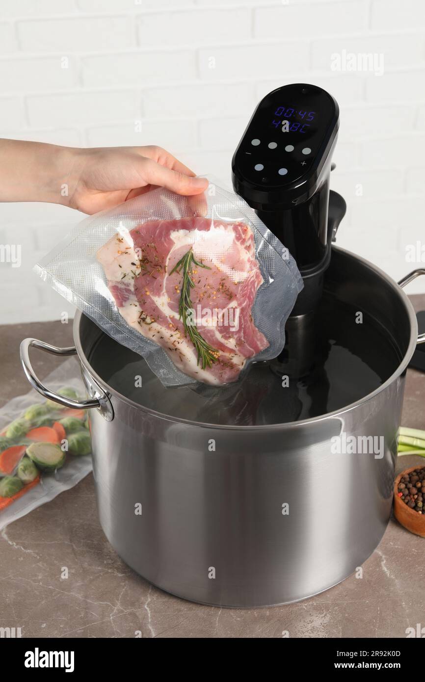 Woman putting vacuum packed meat into pot with sous vide cooker