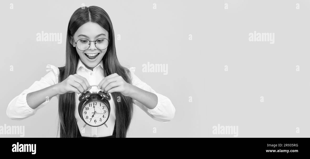 amazed child in school uniform and glasses with alarm clock showing time, school time. Teenager child with clock alarm, horizontal poster. Banner Stock Photo