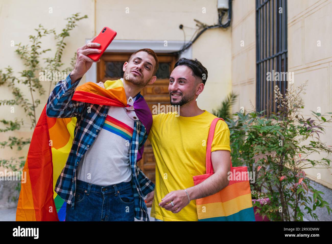 Two gay friends exude happiness as they snap a selfie outside their house,  adorned with colorful LGBT flags, bags, shirts, and more Stock Photo - Alamy