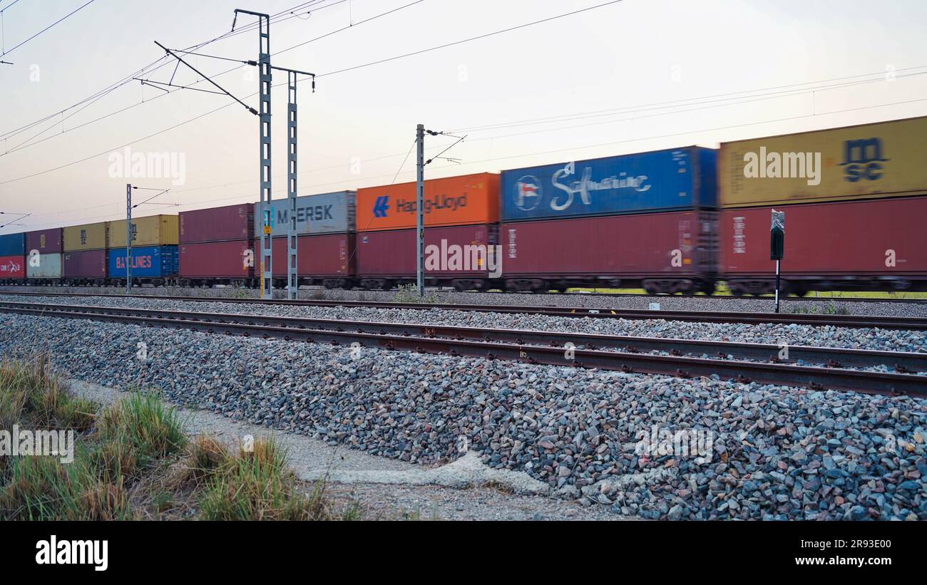 Freight train with cargo containers passing by countryside. Train wagons carrying cargo containers for shipping companies. Distribution and freight tr Stock Photo