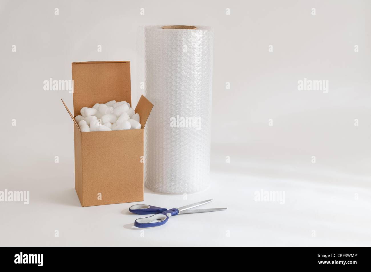 Cardboard box isolated on the white background filled with packing peanuts, bubble wrap and scissors Stock Photo