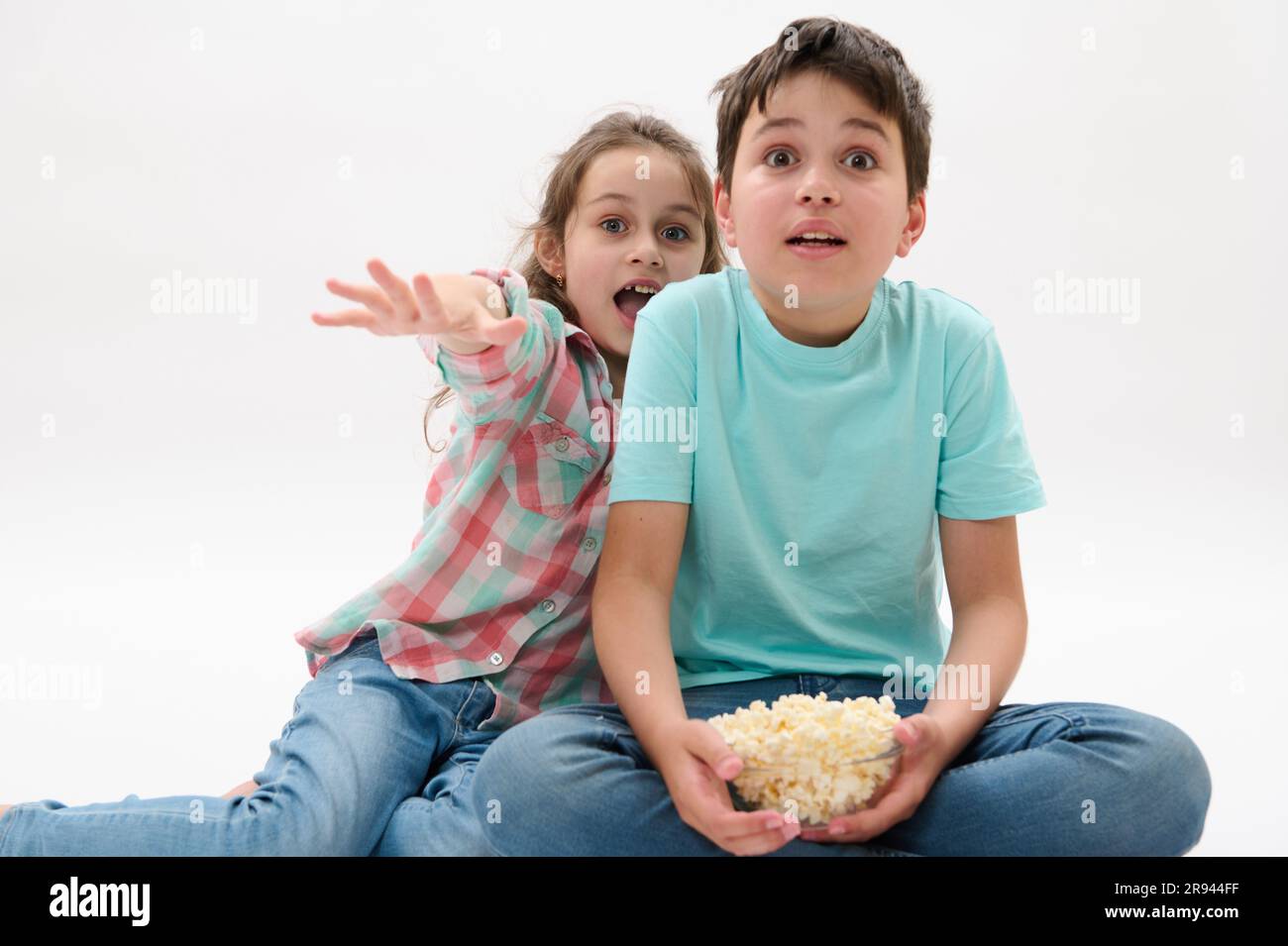 Adorable children with bowl of popcorn, watching scary or fantasy movie, expressing fright and fear on white background Stock Photo