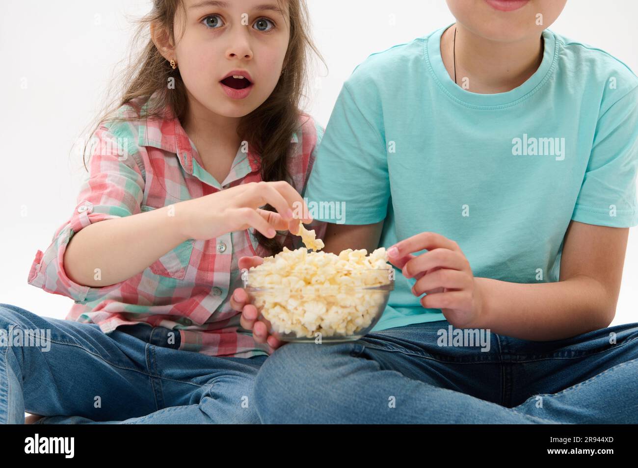 Cropped view kids with a bowl of popcorn, looking fascinated while watching movie, isolated on white studio background Stock Photo